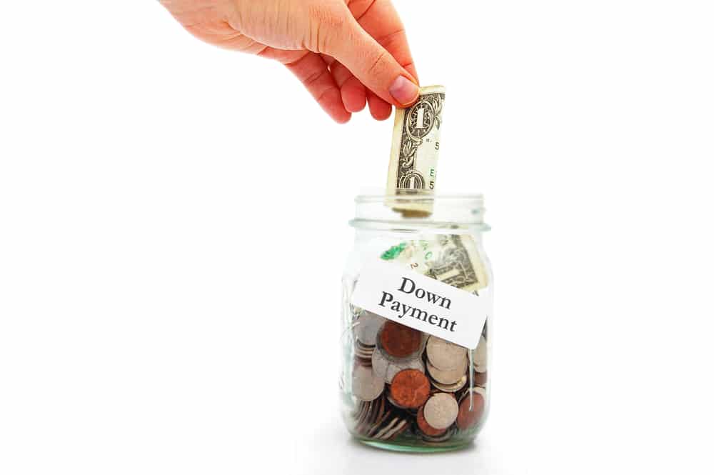 hand putting money into a down payment jar home buying concept