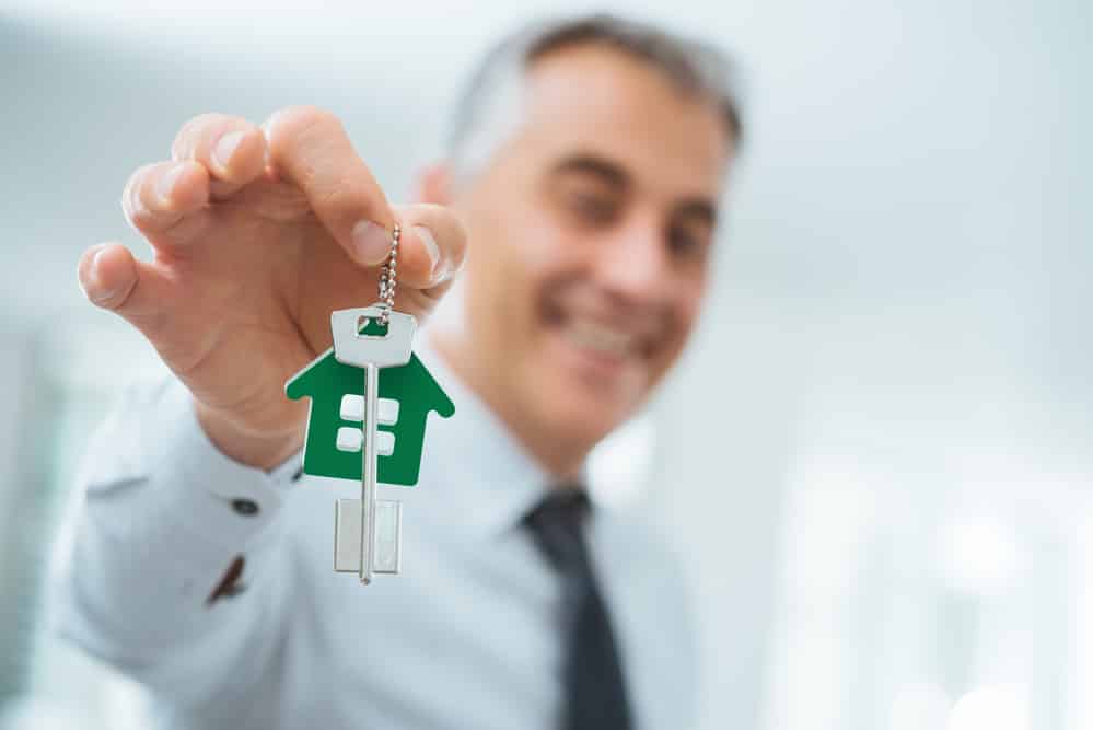 Confident real estate agent holding your new house keys and smiling at camera